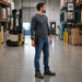Worker wearing an Agoz Cognex DataMan 8700 holster during warehouse verification work with cartons, paperwork, and a handheld device on a loading dock workstation.