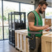 Worker wearing an Agoz belt-mounted scanner holster records crate information on a clipboard while carrying a trigger-handle scanner at a loading dock workstation.
