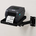TSC desktop label printer on an AgozTech black wall mount printer shelf with adjustable arm, printing a barcode label against a light wall.