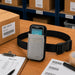 Gray Unitech waist belt pouch displayed on a warehouse pick station with a compact scanner, pick list, barcode labels, and order processing materials.