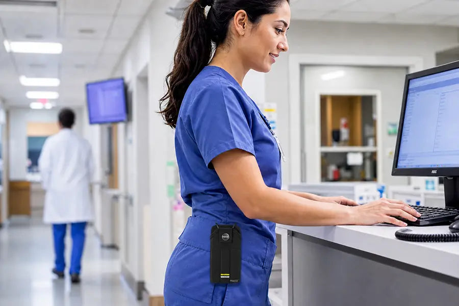 Healthcare worker wearing an Ascom DECT handset snap closure case clipped to scrubs at a hospital workstation.