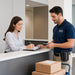 Delivery worker wearing the leather Honeywell handheld scanner case on a belt while checking in at a reception counter with packages on a cart.